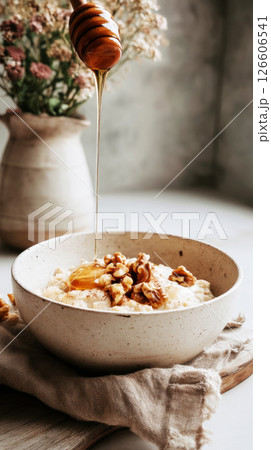Warm oats topped with bananas and walnuts create a cozy breakfast in a softly lit kitchen. Honey drizzles add a touch of sweetness to this seasonal meal 126606541