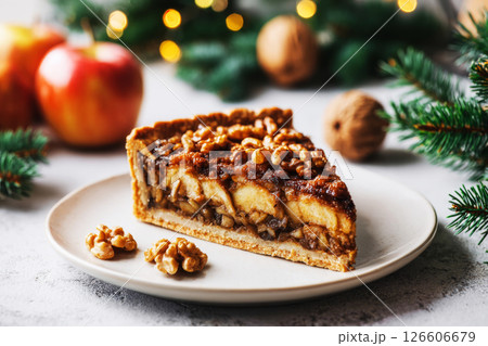 Enjoy a slice of warm apple walnut pie set on a white plate, with bright red apples and twinkling lights in the background, creating a cozy seasonal breakfast atmosphere 126606679
