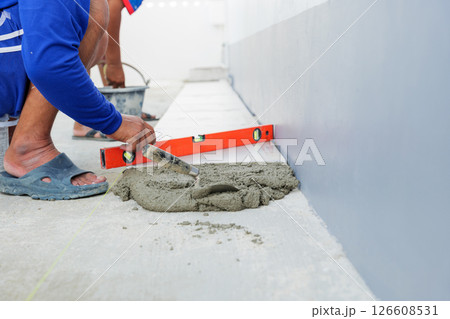 A worker smooths a layer of gray mortar, creating an even foundation for securely setting floor tiles in place. A worker smooths a layer of gray mortar, creating an even foundation for securely setting floor tiles in place. 126608531