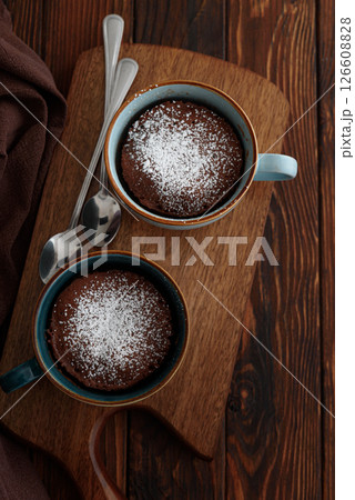 Two chocolate mug cake under sugar icing on dark wooden table. Easy homemade dessert. Mugcake from microwave. Top view Two chocolate mug cake under sugar icing on dark wooden table. Easy homemade dessert. Mugcake from microwave. Top view 126608828