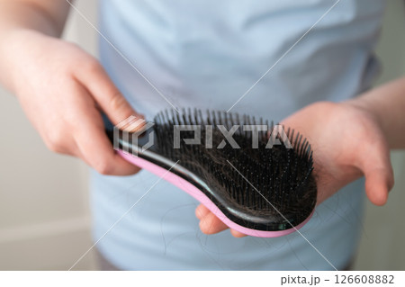 Hands of girl holding black comb with much hairs after hair loss. Problem hair because of stress. 126608882