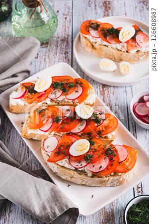 Sandwiches with ricotta, tomato, radish and egg on a plate on a table vertical view 126608987