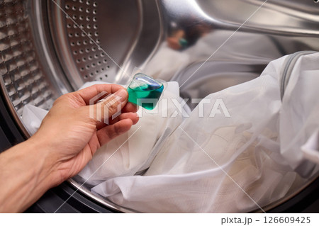 A hand is holding a colorful laundry pod as it is placed into a washing machine for cleaning A hand is holding a colorful laundry pod as it is placed into a washing machine for cleaning 126609425