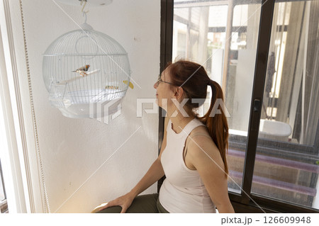 Woman looking at zebra finch in hanging cage at home 126609948