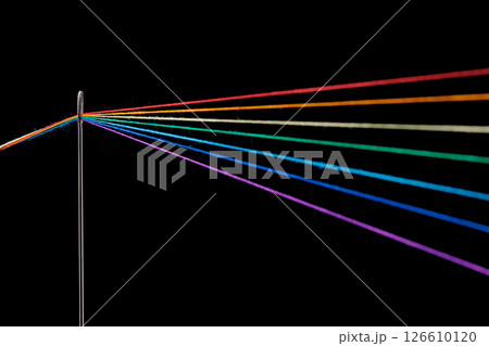 multi-colored threads for sewing in the form of a rainbow pass through an antique needle on a black background multi-colored threads for sewing in the form of a rainbow pass through an antique needle on a black background 126610120