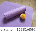 Sports equipment: purple myofascial release roller and yellow spiky ball on the background of yoga, pilates and fitness mat lying on wooden floor. Healthy lifestyle items 126610560