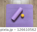 Top view of sports equipment: yellow massage ball, purple myofascial release roller and fitness yoga mat lying on wooden floor. Fitness and healthy lifestyle equipment 126610562