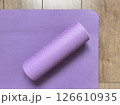 Top view of purple myofascial release roller on fitness yoga mat lying on wooden floor. Sports equipment for fitness, massage and healthy lifestyle 126610935