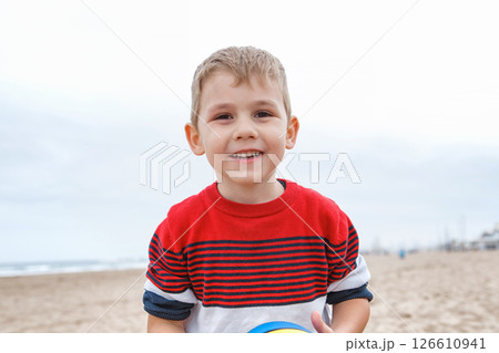 Young Boy Playing With a Colorful Beach Ball on a Sandy Shoreline During a Cloudy Afternoon 126610941