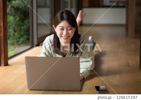 和風の古民家の縁側で寝転がってパソコンをする女性　田舎でのリモートワークや地方移住のイメージ 126615397