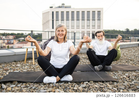 Senior man and woman practicing yoga in lotus pose on rooftop terrace outdoors. 126616883