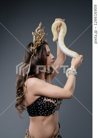 Woman in traditional attire performs with a snake in a studio setting 126616909