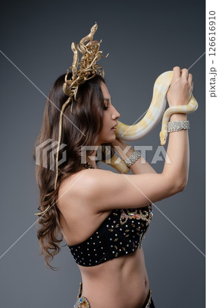 Woman in elegant costume interacts with a snake during a performance 126616910