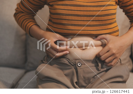 Cropped shot of woman touching and squeezing her fat belly. Cropped shot of woman touching and squeezing her fat belly. 126617441