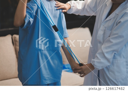 Doctor physiotherapist assisting a male patient while giving exercising treatment on stretching his arm with exercise band in the clinic, Rehabilitation physiotherapy concept Doctor physiotherapist assisting a male patient while giving exercising treatment on stretching his arm with exercise band in the clinic, Rehabilitation physiotherapy concept 126617482