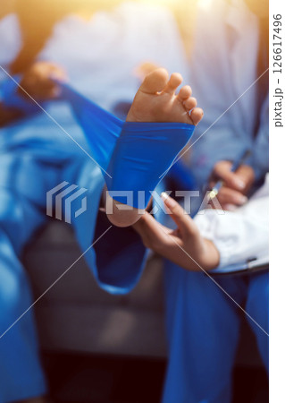 Confident physical therapist helps patient use resistance band stretching out his leg in clinic room. 126617496