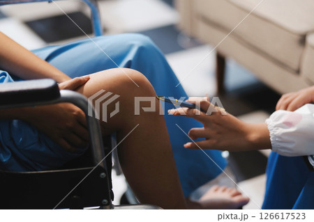 A female doctor examines an elderly patient with knee pain due to arthritis. The patient is being assisted in recovery, focusing on pain management and improving mobility. 126617523