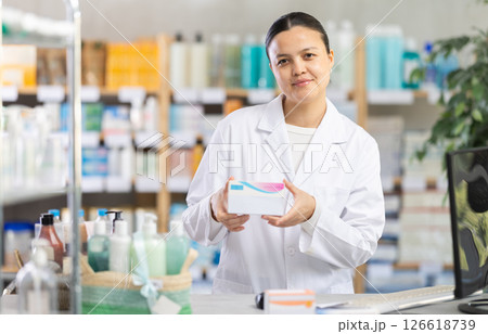 Female pharmacist offering box of pills at pharmacy counter Female pharmacist offering box of pills at pharmacy counter 126618739