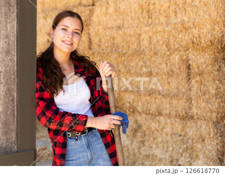 Portrait of a young positive farmer girl standing near haystacks 126618770