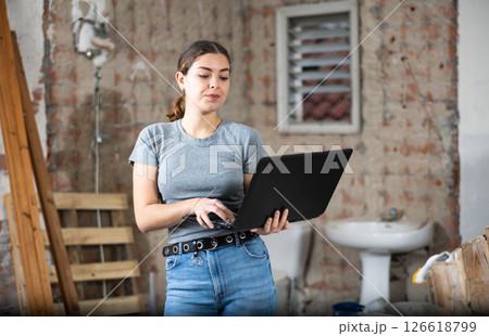 Female designer using laptop in apartment during repair works Female designer using laptop in apartment during repair works 126618799