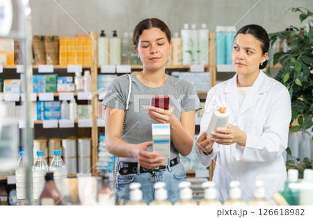 Young girl scanning QR on cream while pharmacist offering in drugstore Young girl scanning QR on cream while pharmacist offering in drugstore 126618982