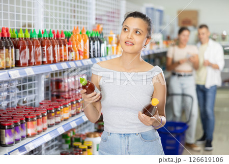 Woman is holding bottle with sauce in chinese shop. Young positive female customer choosing spicy sauce in supermarket Woman is holding bottle with sauce in chinese shop. Young positive female customer choosing spicy sauce in supermarket 126619106