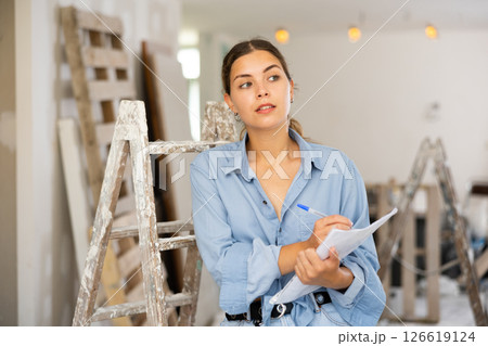 Woman with documents in her hands checks the quality of the completed repairs in cottage room 126619124