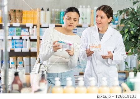 Portrait of young woman pharmacist helping asian female client choosing pill box and making decisions about pharmaceuticals and health care at pharmacy Portrait of young woman pharmacist helping asian female client choosing pill box and making decisions about pharmaceuticals and health care at pharmacy 126619133