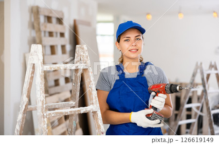 Portrait of a contented young female builder in blue overalls holding screwdriver Portrait of a contented young female builder in blue overalls holding screwdriver 126619149