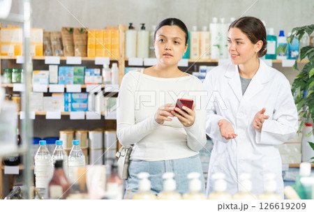 Middle-aged woman scrolling phone while looking for something and pharmacist consulting Middle-aged woman scrolling phone while looking for something and pharmacist consulting 126619209