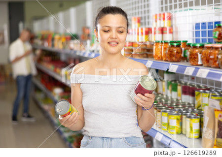 Young woman chooses canned food in store 126619289