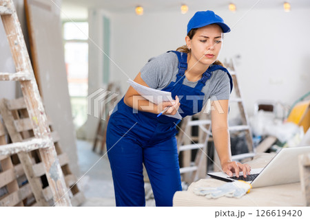 Woman builder checking documentation, using laptop Woman builder checking documentation, using laptop 126619420