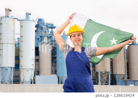 Young female engineer in helmet waving state flag of Pakistan while standing in front of big tanks at chemical plant 126619424