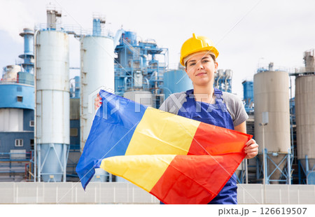Happy girl in work clothes and hardhat with flag of romania standing in front of industrial scenery Happy girl in work clothes and hardhat with flag of romania standing in front of industrial scenery 126619507
