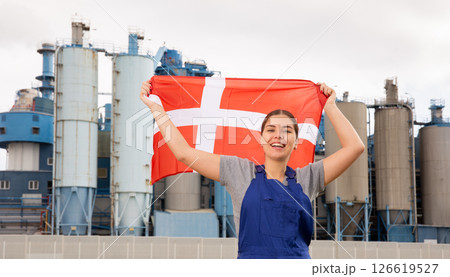 Happy young woman worker with flag of Denmark against background of factory Happy young woman worker with flag of Denmark against background of factory 126619527