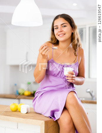 Portrait of positive girl in nightdress eating yogurt at home Portrait of positive girl in nightdress eating yogurt at home 126619547