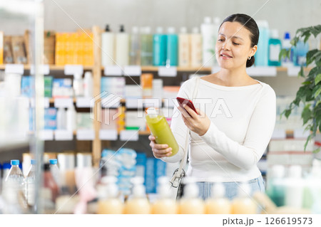 Middle-aged woman scanning QR-code on shampoo or gel in drugstore 126619573