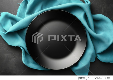 Empty matte black plate on turquoise fabric napkin over dark textured surface. Minimal top-down composition perfect for menu mockups, food blogs, restaurants, or elegant culinary presentations 126620736