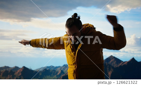 Pleased hiker celebrating his personal achievement on mountain top, showing determination for beautiful landscape and sightseeing. Adventure seeker doing a dance with satisfaction. Camera A. 126621322