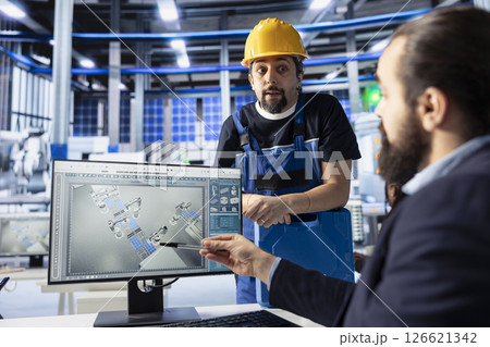 Manager in photovoltaics factory talking with worker, diagnosing malfunctioning systems, pointing to PC screen. Solar panels manufacturing plant experts doing brainstorming to reduce downtime 126621342