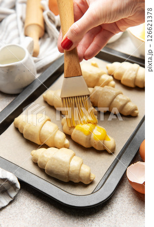 Baker brushing egg yolk on raw croissants on baking sheet Baker brushing egg yolk on raw croissants on baking sheet 126621378
