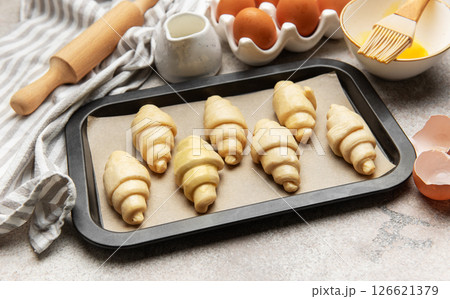 Baking tray with raw croissants, waiting to be cooked, surrounded by kitchen utensils 126621379