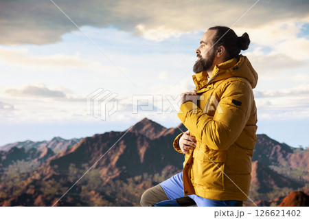 Nature lover stands at the edge of a breathtaking mountain range, looking at the scenic background of towering peaks and vast sky. Young man enjoying adventure and outdoor exploration. Nature lover stands at the edge of a breathtaking mountain range, looking at the scenic background of towering peaks and vast sky. Young man enjoying adventure and outdoor exploration. 126621402