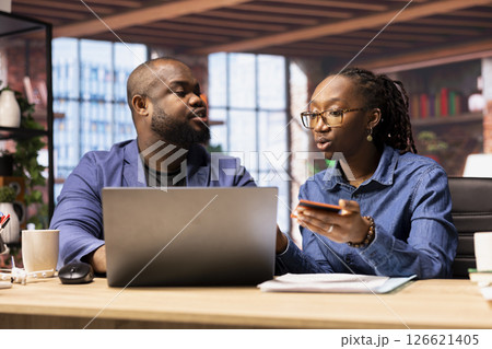 Mature couple dealing with online banking together at home office in the loft, setting up payments and confirming money transfer. Pleased man and woman enjoy online shopping on laptop. Mature couple dealing with online banking together at home office in the loft, setting up payments and confirming money transfer. Pleased man and woman enjoy online shopping on laptop. 126621405