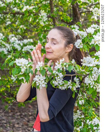 Young woman sneezes in the park against the background of a flowering tree. Allergy to pollen concept. Young woman sneezes in the park against the background of a flowering tree. Allergy to pollen concept. 126623207