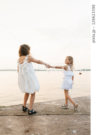 Two young girls are walking on beach, one of them holding the other's hand Two young girls are walking on beach, one of them holding the other's hand 126623398