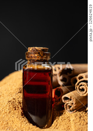 Glass bottle of cinnamon oil on the background of cinnamon sticks and ground cinnamon. 126624619
