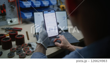 Man Checking Exchange Market Charts on Smartphone and Laptop in Workshop 126624963