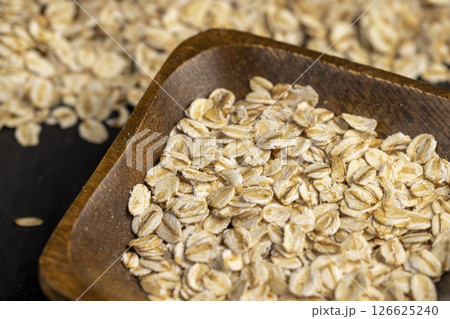 oat flakes into a wooden bowl, oatmeal for quick cooking of porridge 126625240