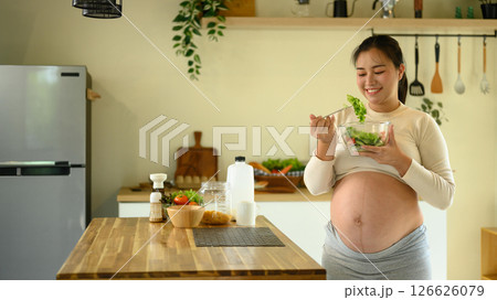 Pregnant woman enjoying a fresh salad in a modern kitchen 126626079